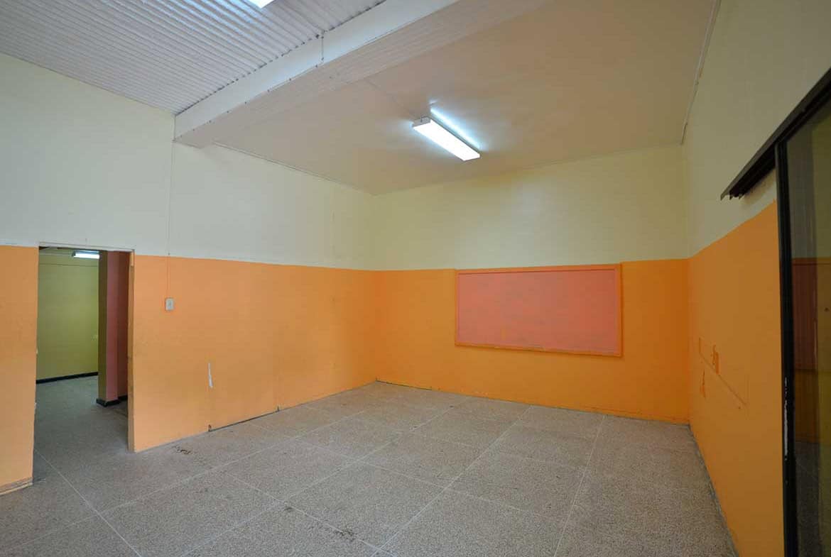 Cornerstone- Empty room with orange walls and fluorescent lighting in Curepe.