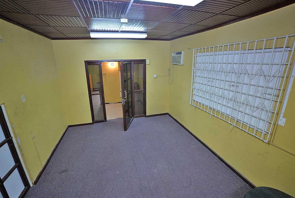 Cornerstone- Empty office room with yellow walls, gray carpet, and window security bars.