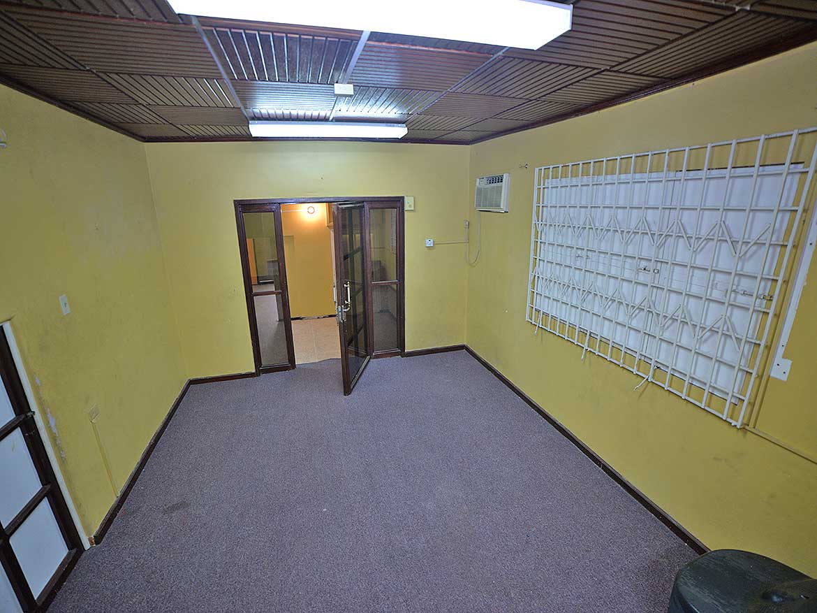 Cornerstone™ Office Space in Curepe Cornerstone- Empty office room with yellow walls, gray carpet, and window security bars.