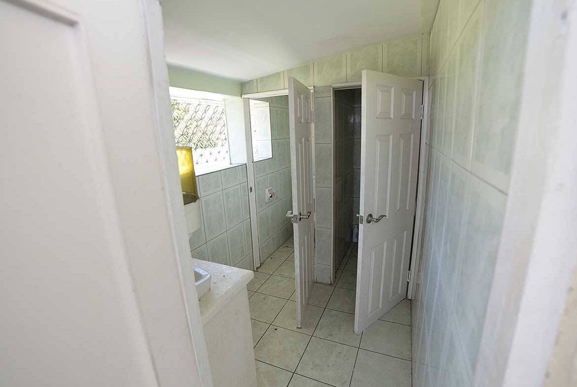 Cornerstone- Bathroom with open door, tiled walls and small window in Curepe.