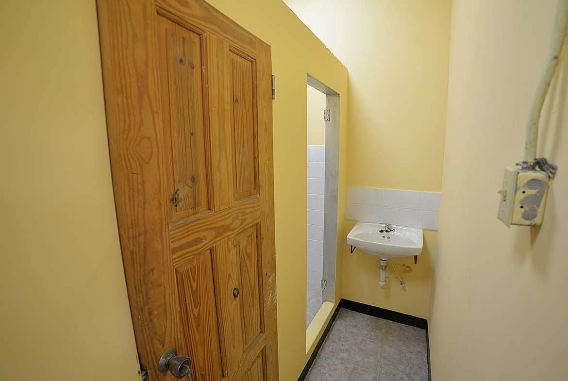 Cornerstone- Small restroom with wooden door and wall-mounted sink in St James Street building.
