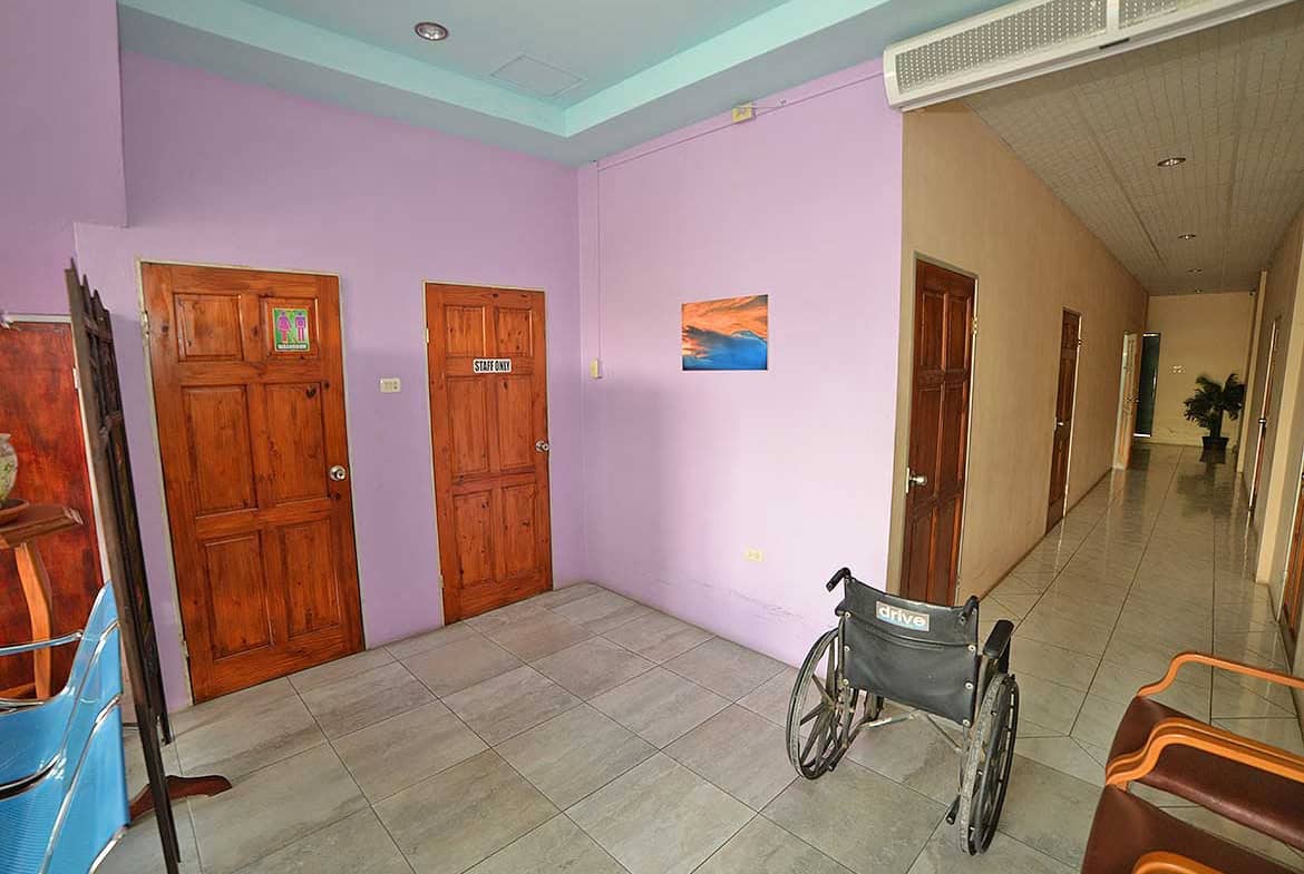 Cornerstone- Wheelchair in a corridor of a healthcare facility with wooden doors and pastel-colored walls.