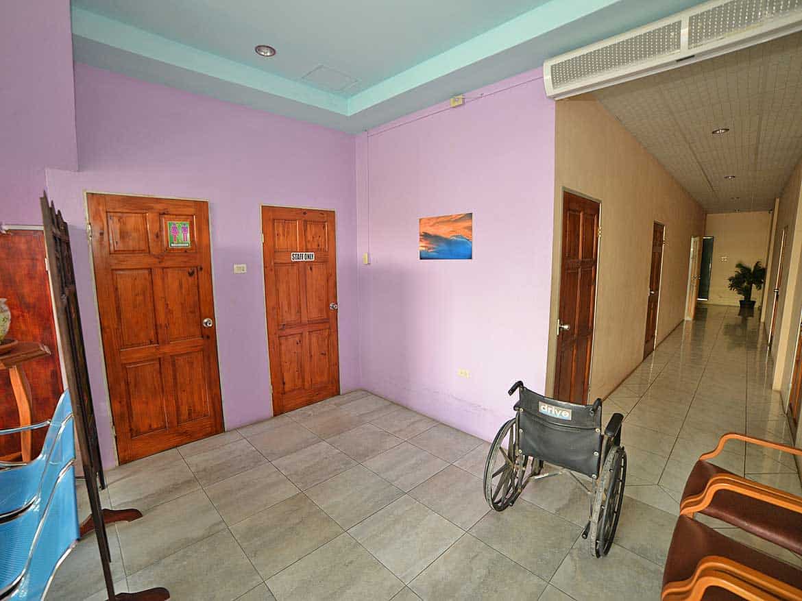Interior of a healthcare facility corridor Cornerstone- Wheelchair in a corridor of a healthcare facility with wooden doors and pastel-colored walls.