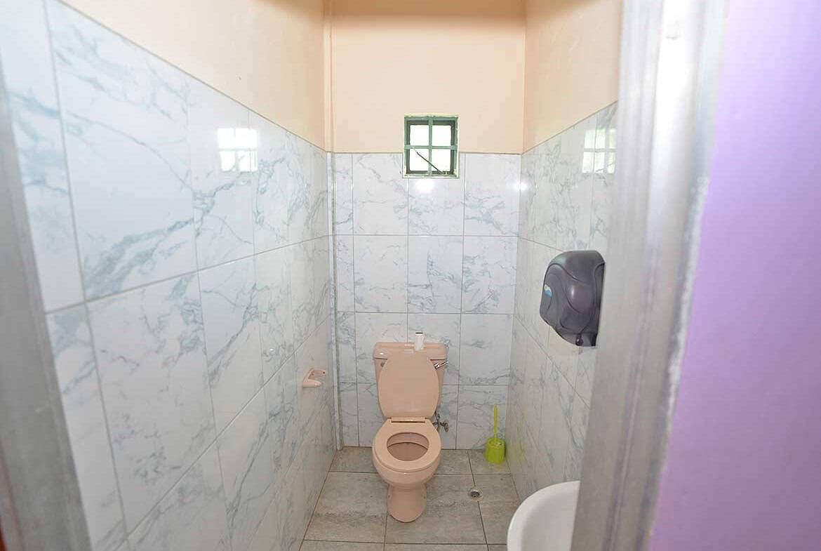 Cornerstone- Small bathroom with toilet, wall-mounted paper towel dispenser, and window.