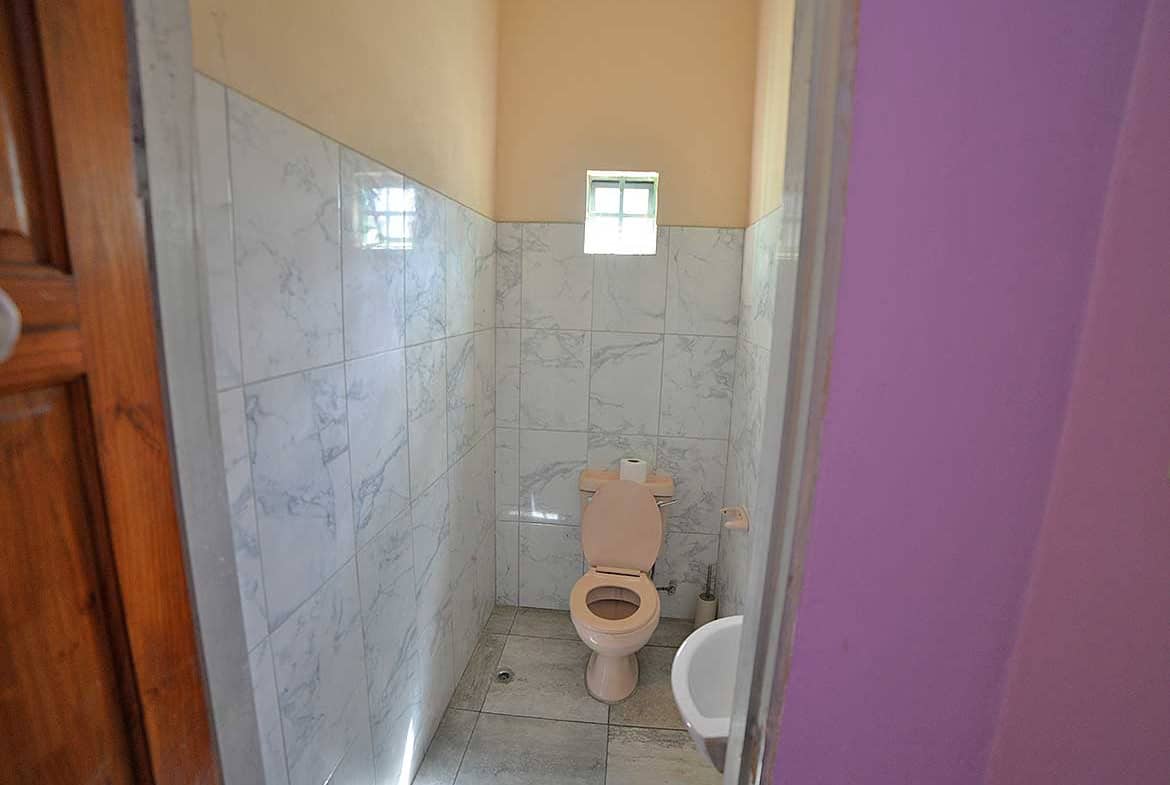 Cornerstone- Compact bathroom with toilet, small window, and tiled walls.