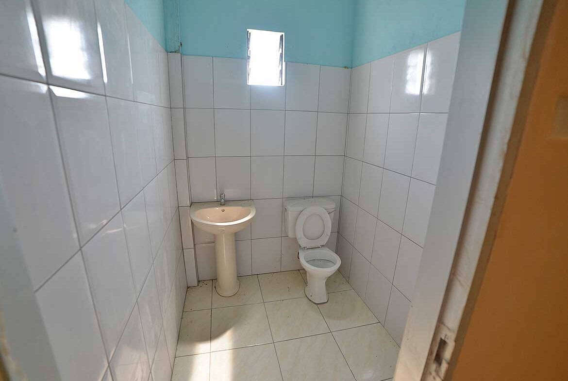Cornerstone- Small bathroom with white tiles, a toilet, and a sink under a window.