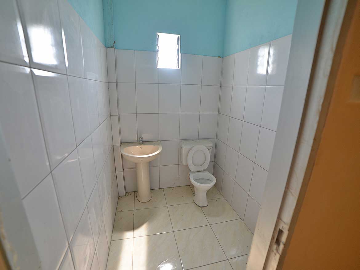 Restroom Renovation at Bonne Aventure Road Cornerstone- Small bathroom with white tiles, a toilet, and a sink under a window.