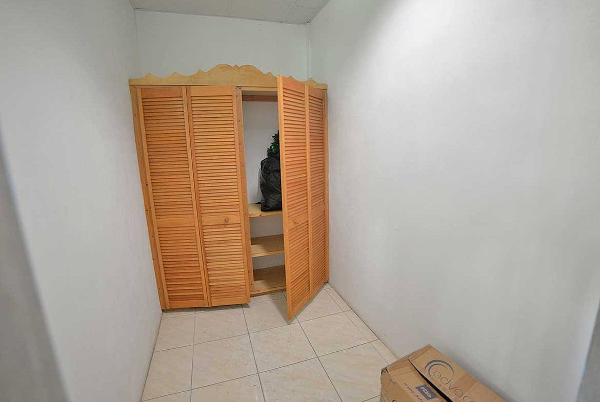 Cornerstone- Small storage closet with wooden louvered doors in a white room.