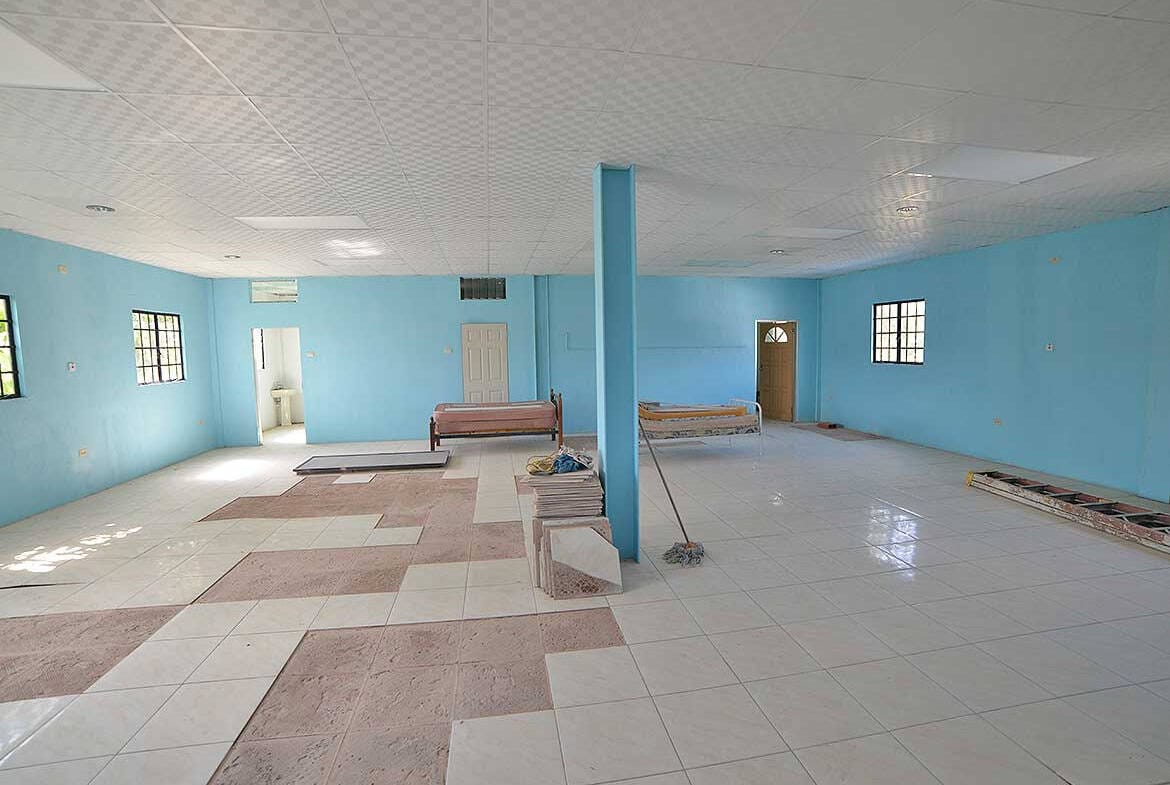 Cornerstone- Large community hall with blue walls and tiled floor, benches, and windows.