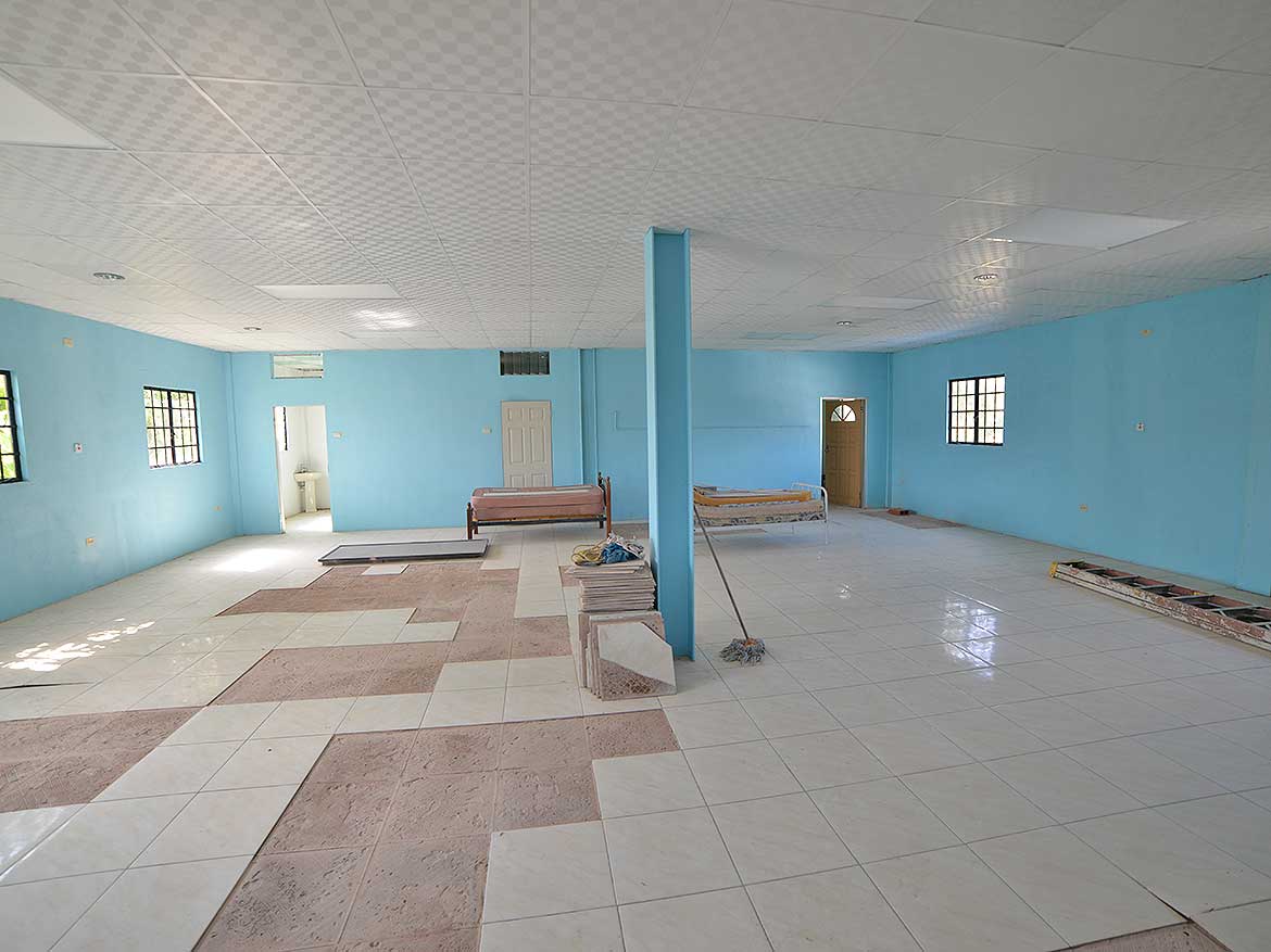 Interior of a Spacious Community Hall Cornerstone- Large community hall with blue walls and tiled floor, benches, and windows.