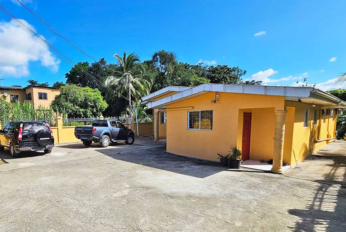 Cornerstone- Yellow building with parking lot and tropical trees under blue sky.