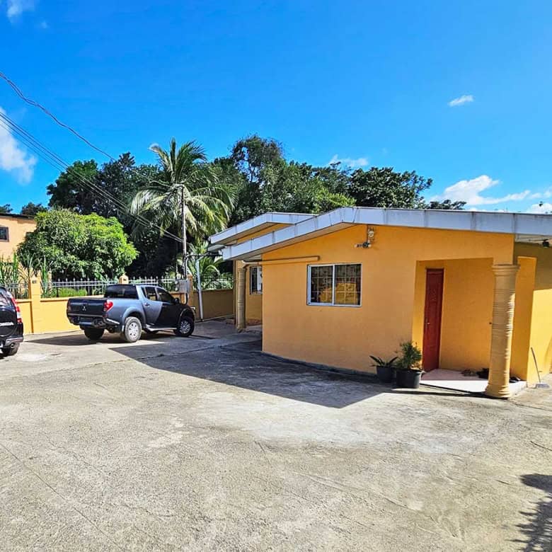 Cornerstone- Yellow building with parking lot and tropical trees under blue sky.