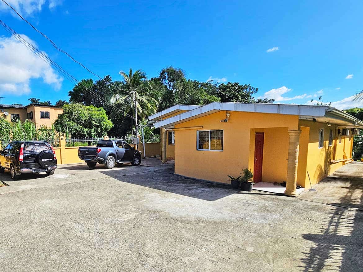 Cornerstone- Yellow building with parking lot and tropical trees under blue sky.