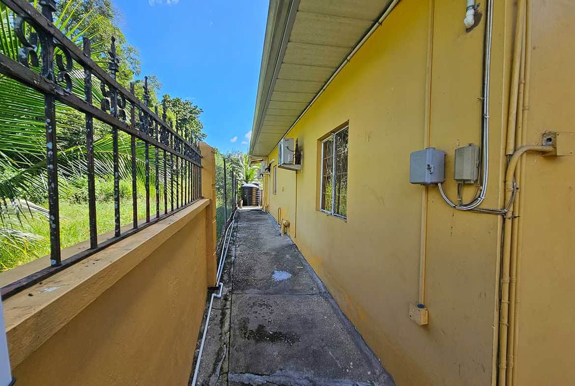 Cornerstone- Side view of a yellow apartment building on Calcutta Road with electrical boxes and a fence.
