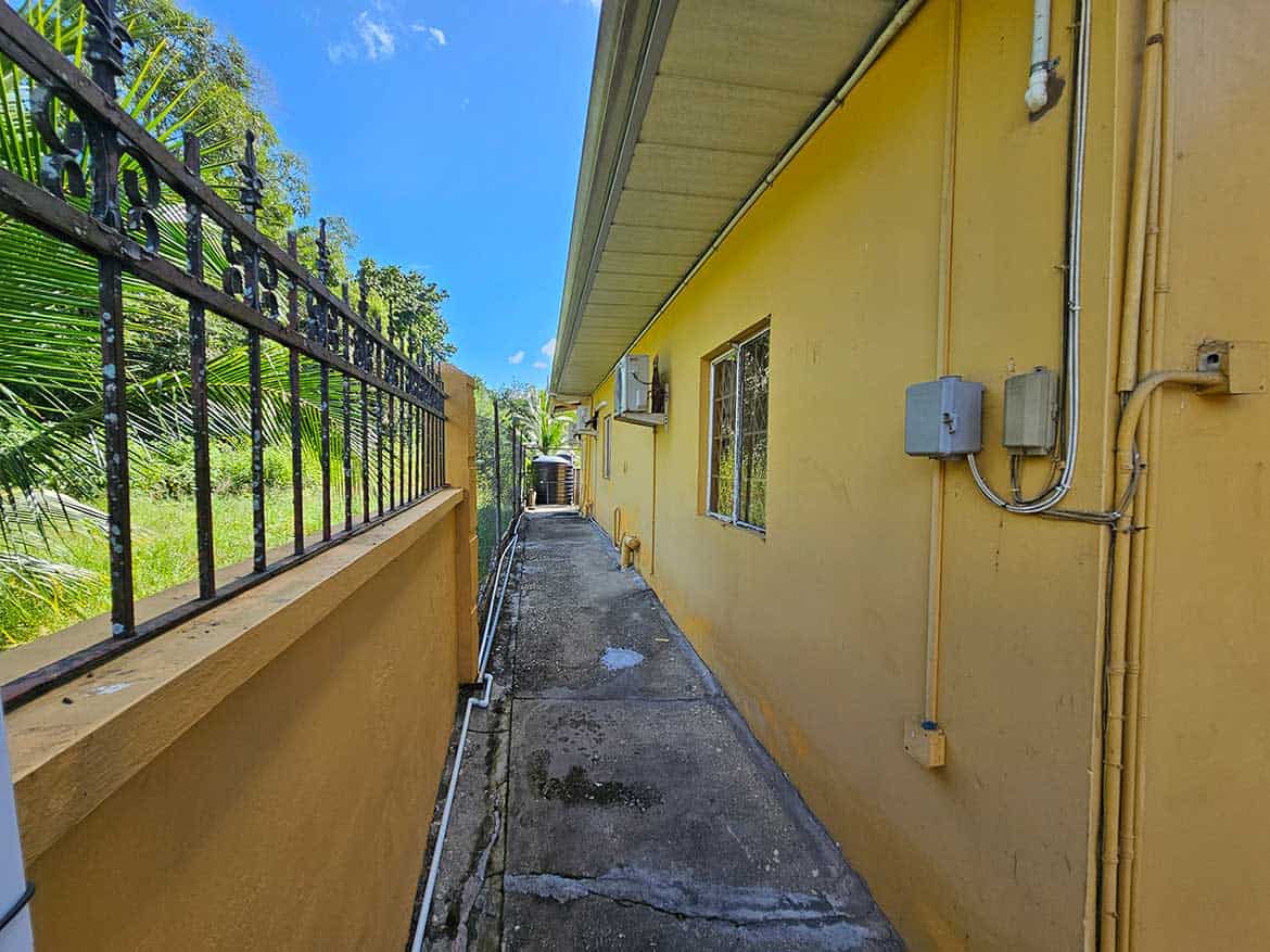 Calcutta Road Apartment Exterior View Cornerstone- Side view of a yellow apartment building on Calcutta Road with electrical boxes and a fence.