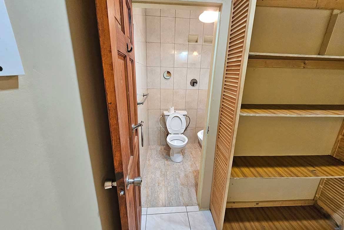 Cornerstone- Compact bathroom with toilet and wooden storage shelves in a residential space.