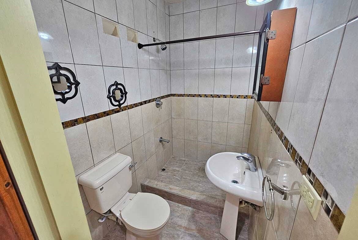 Cornerstone- Compact bathroom with toilet, sink, and tiled walls and floor.