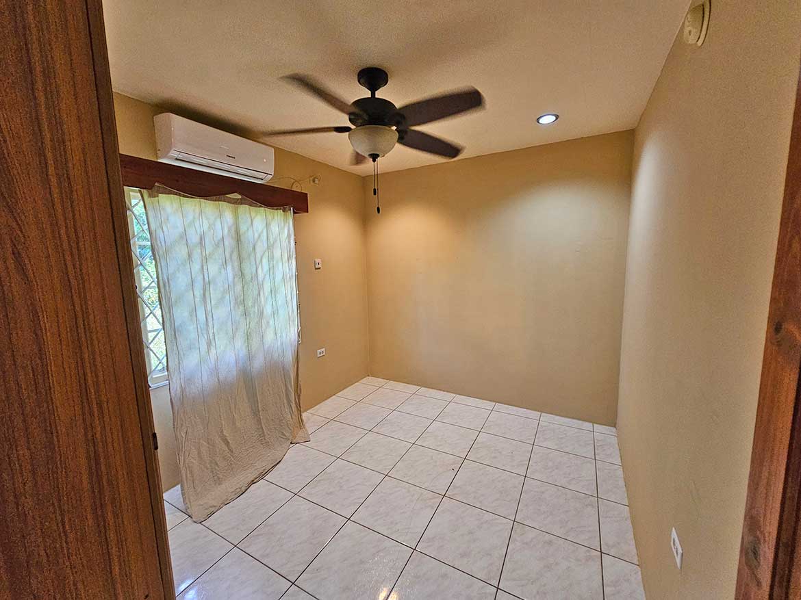 Calcutta Road Apartment Interior Cornerstone- Empty room with ceiling fan, air conditioner, and window with curtains.