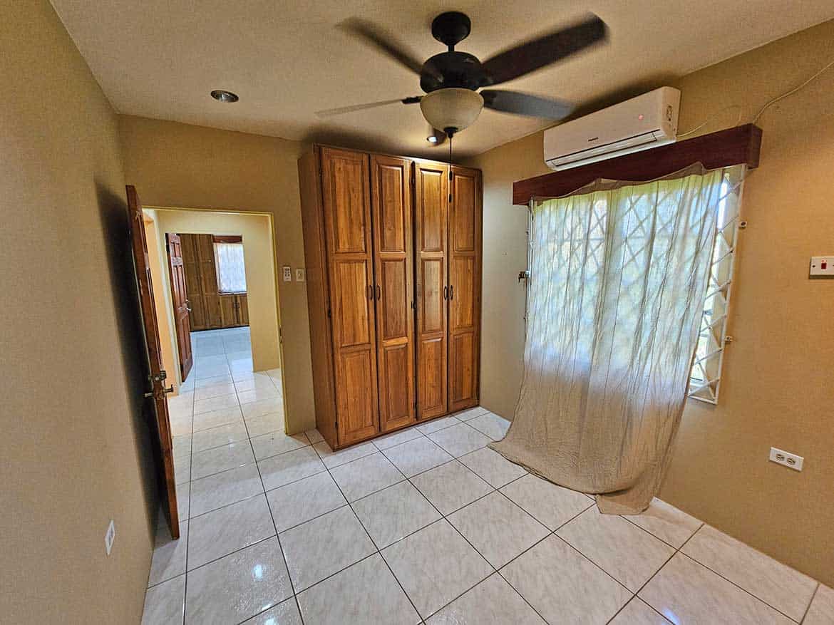 Calcutta Road Apt 1 Interior Cornerstone- Spacious room with wooden wardrobe, ceiling fan, and air conditioner.