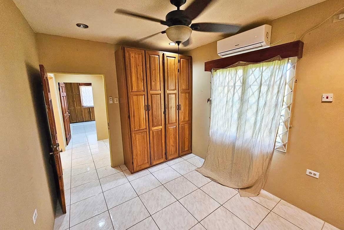 Cornerstone- Interior of a room with wooden wardrobe, ceiling fan, and window with curtains.
