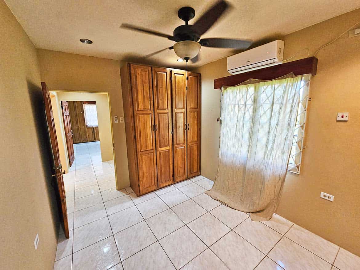 Calcutta Road Apt 1 Interior View Cornerstone- Interior of a room with wooden wardrobe, ceiling fan, and window with curtains.