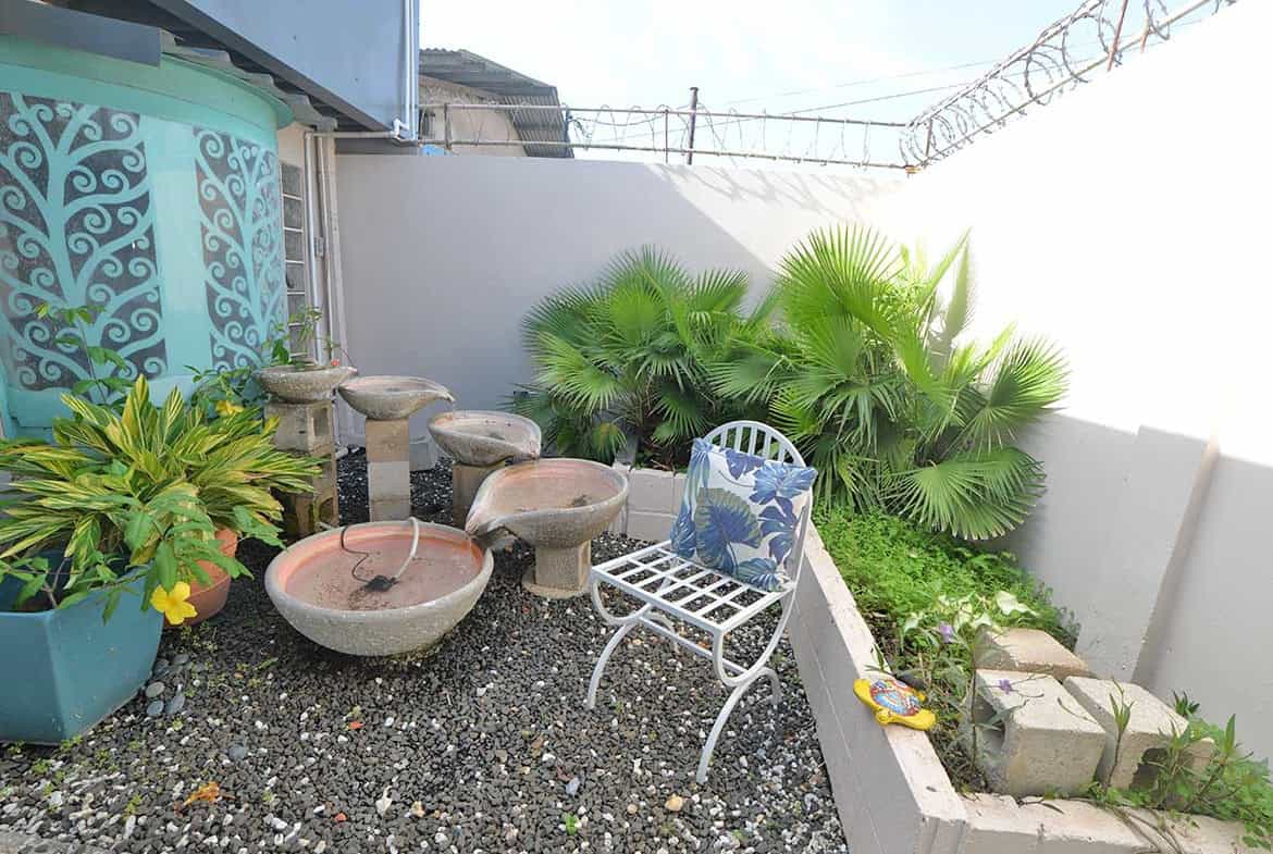Cornerstone- Small outdoor garden with water fountain, plants, and seating area.