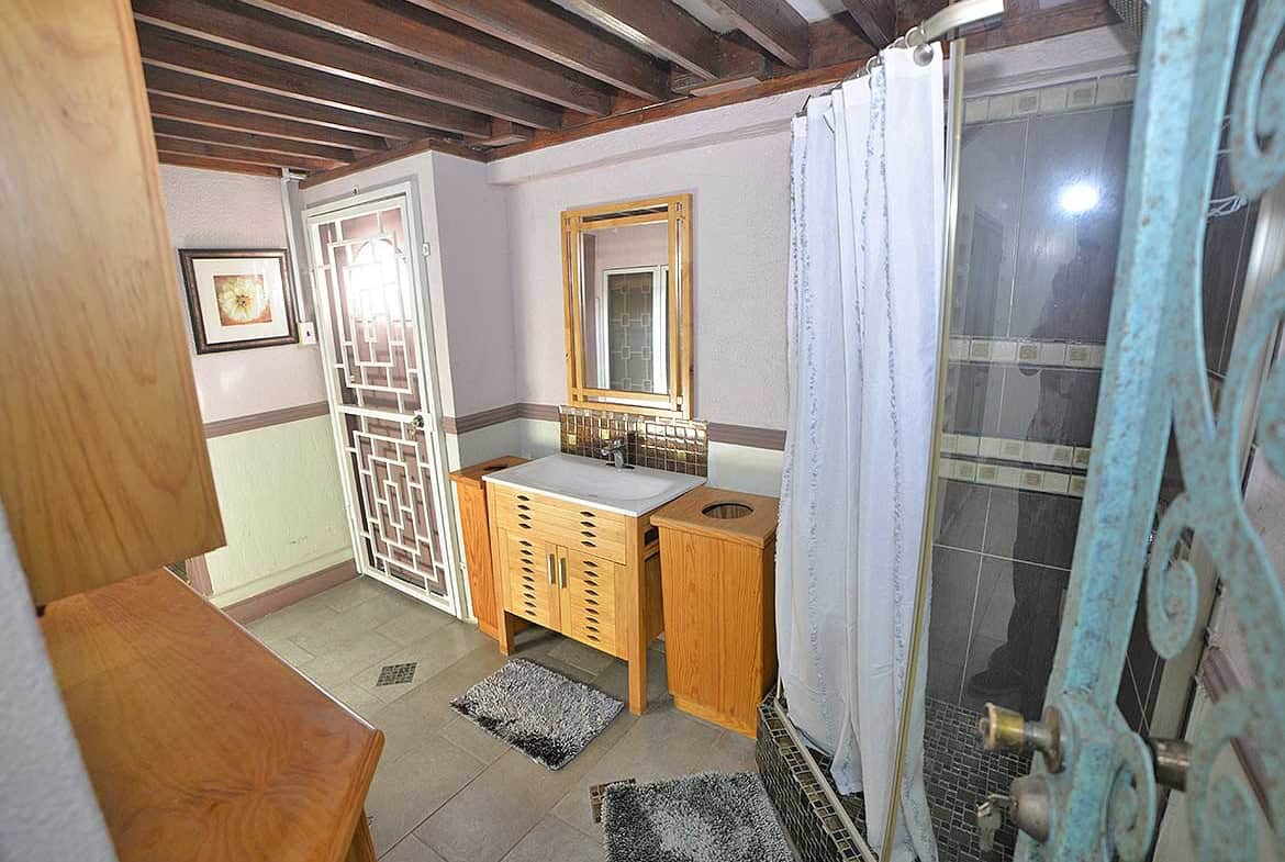 Cornerstone- Small bathroom with wooden accents, mirror, and shower curtain.