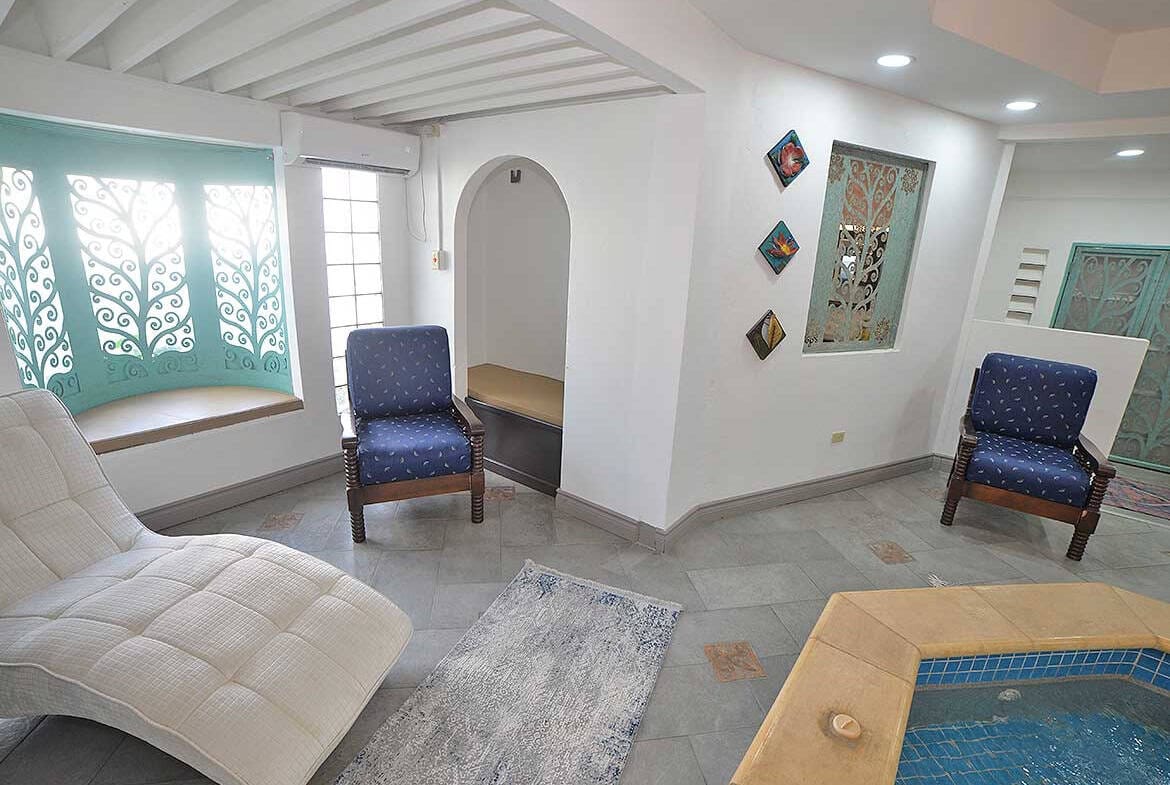 Cornerstone- Bright living room with blue chairs, decorative wall art, and a small pool.