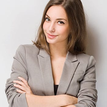 Cornerstone- Confident young woman in gray blazer with arms crossed, smiling at camera.
