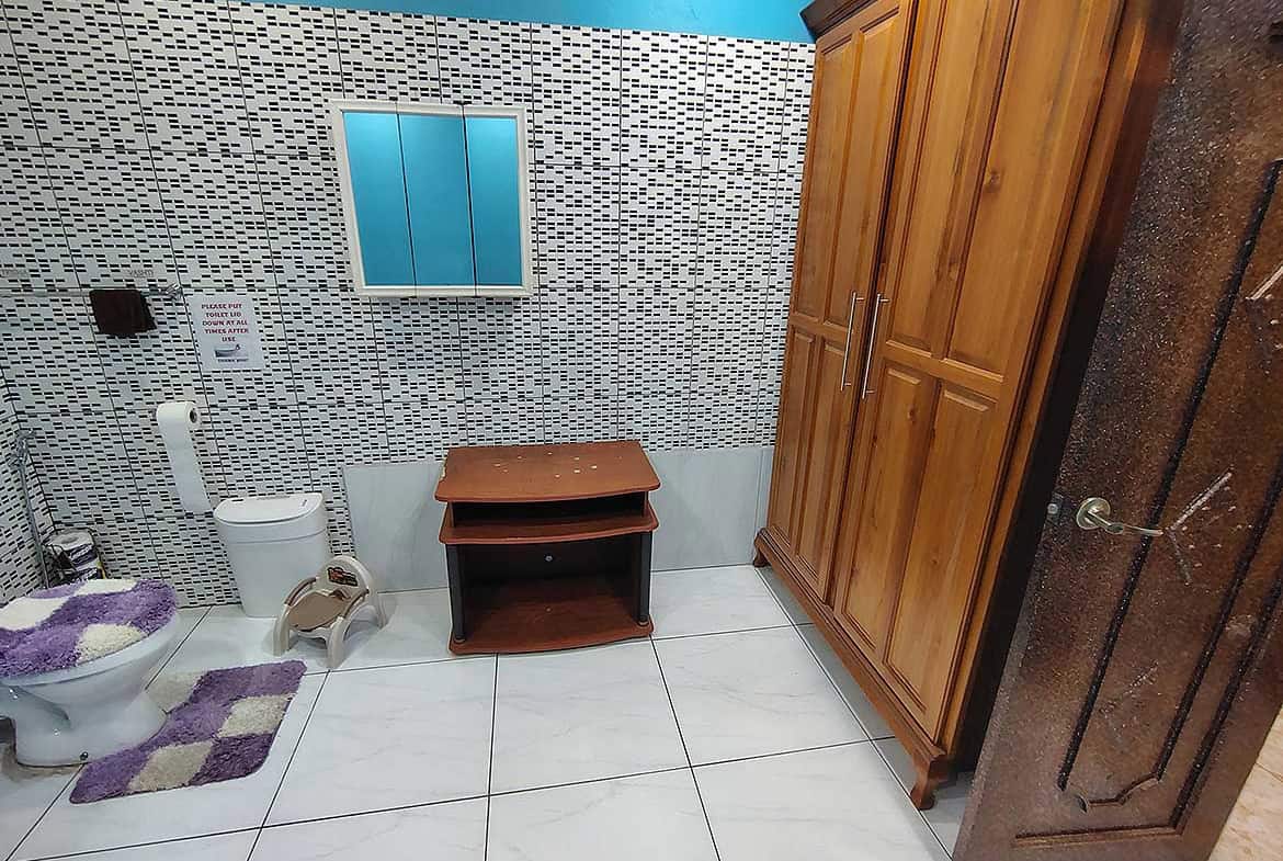 Cornerstone- Bathroom with toilet, wooden cabinet, and tiled wall design.