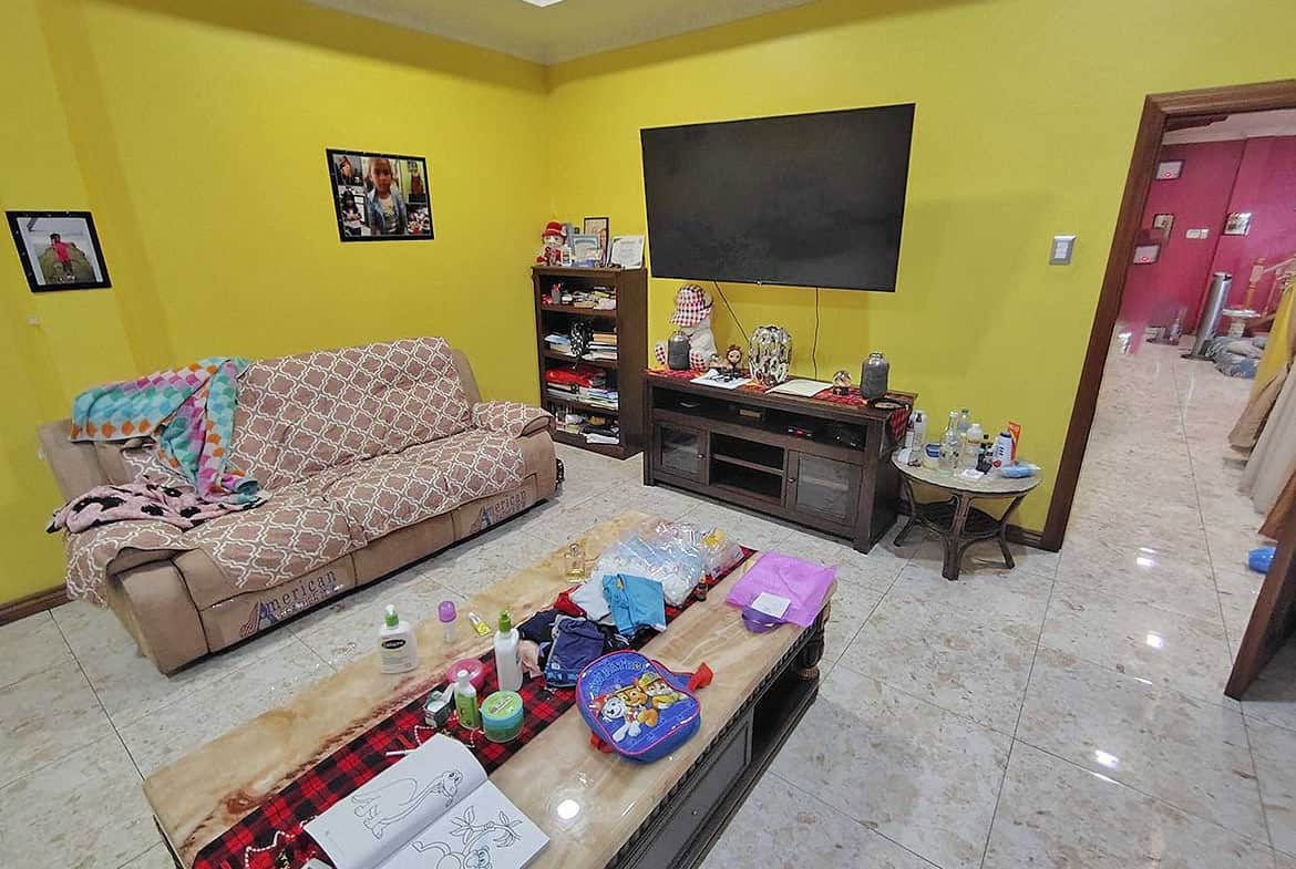Cornerstone- Living room with yellow walls, sofa, TV, and coffee table filled with items.