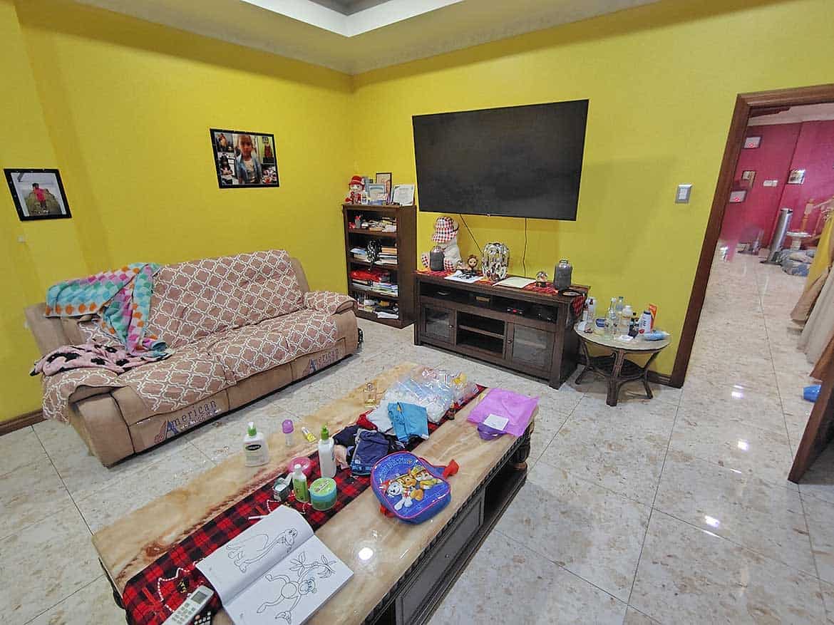 Living Room with TV and Decor Cornerstone- Living room with yellow walls, sofa, TV, and coffee table filled with items.
