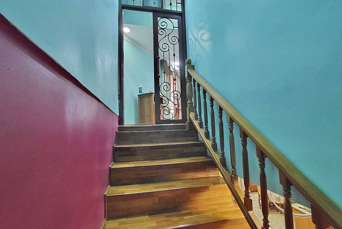 Cornerstone- Colorful interior staircase with wooden steps and decorative iron gate at residence with retail.