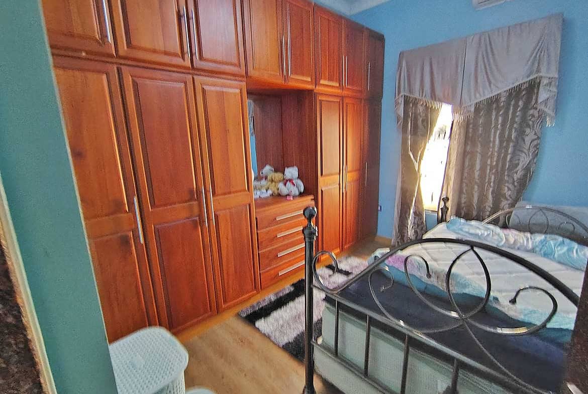 Cornerstone- Cozy bedroom with wooden wardrobe, metal bed frame, and window with curtains.