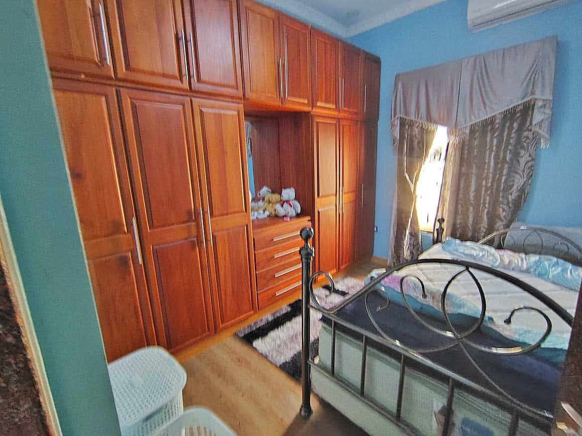 Bedroom with Wooden Wardrobe and Bed Cornerstone- Cozy bedroom with wooden wardrobe, metal bed frame, and window with curtains.