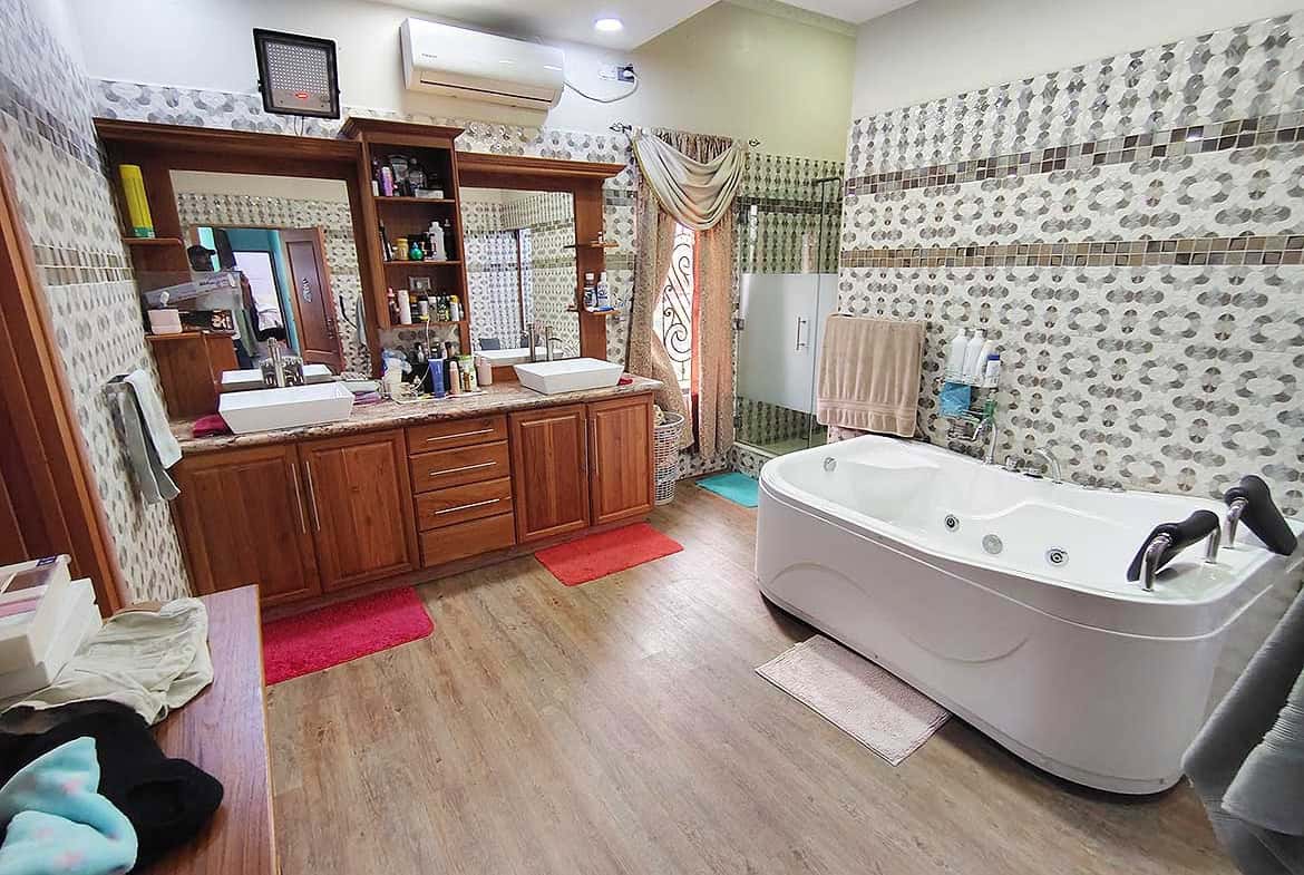 Cornerstone- Spacious bathroom with Jacuzzi tub, wooden vanity, and decorative wall tiles.