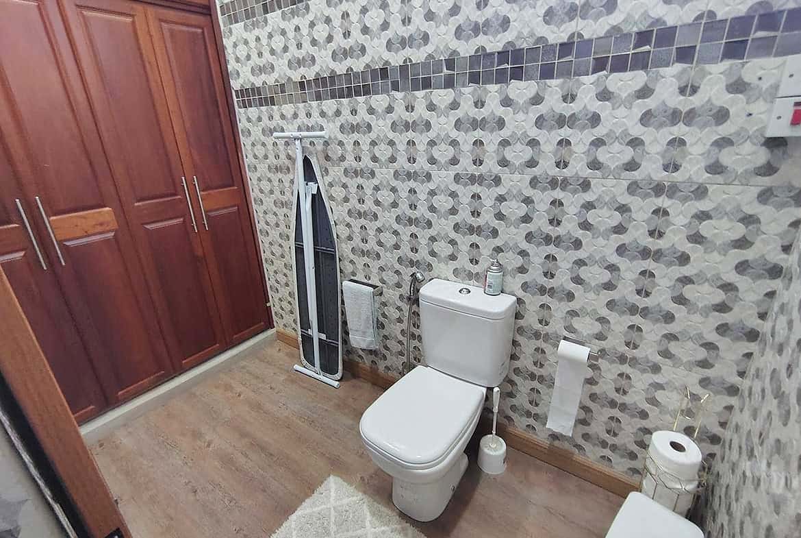 Cornerstone- Contemporary bathroom with wooden cabinets, toilet, and patterned wall tiles.