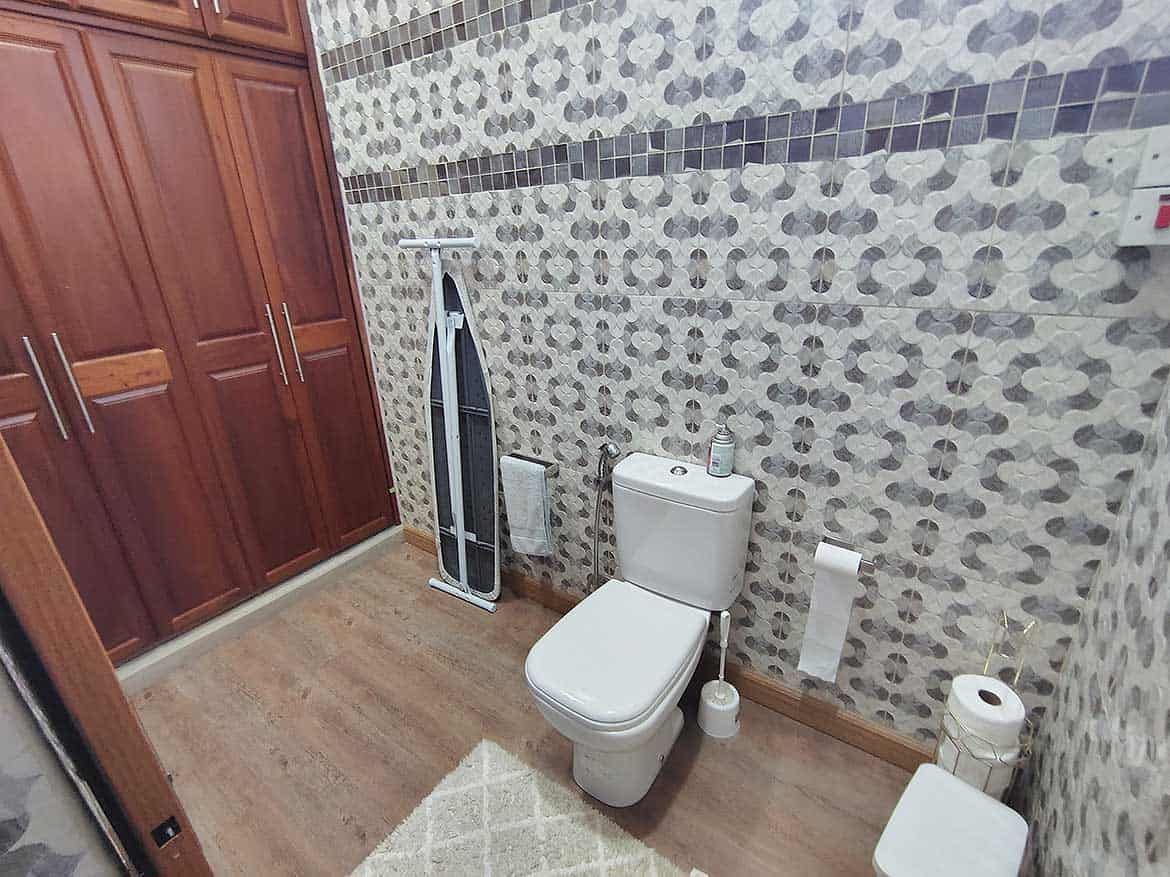 Modern Bathroom with Storage and Toilet Cornerstone- Contemporary bathroom with wooden cabinets, toilet, and patterned wall tiles.