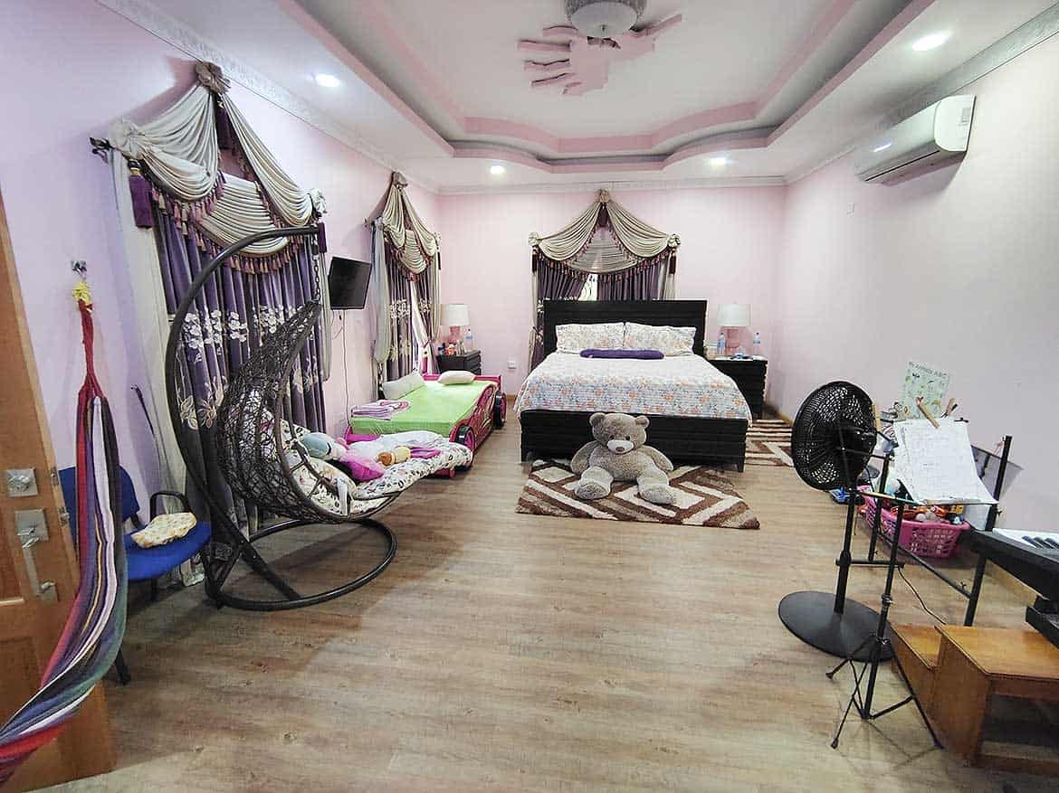 Spacious Bedroom with Elegant Decor Cornerstone- Large bedroom with pink walls, canopy bed, and cozy seating area.