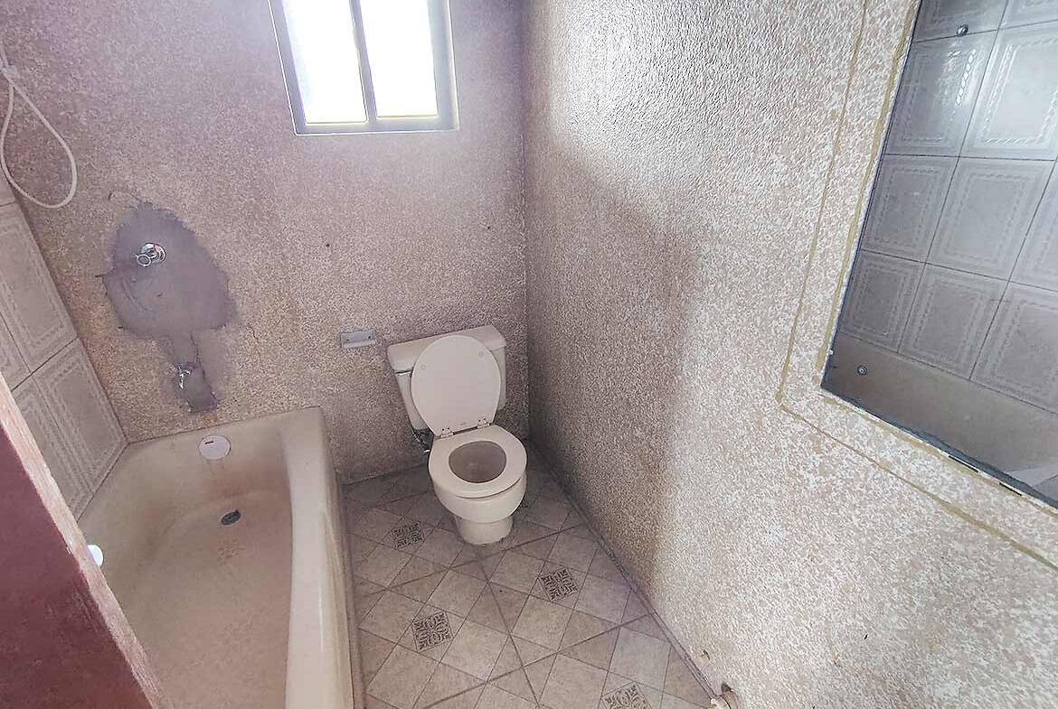 Cornerstone- Small bathroom with bathtub, toilet, and mirror in a modest setting.
