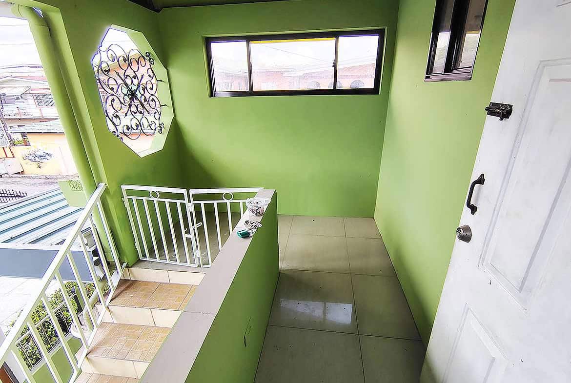 Cornerstone- Bright green balcony with white railing and large window in El Socorro.