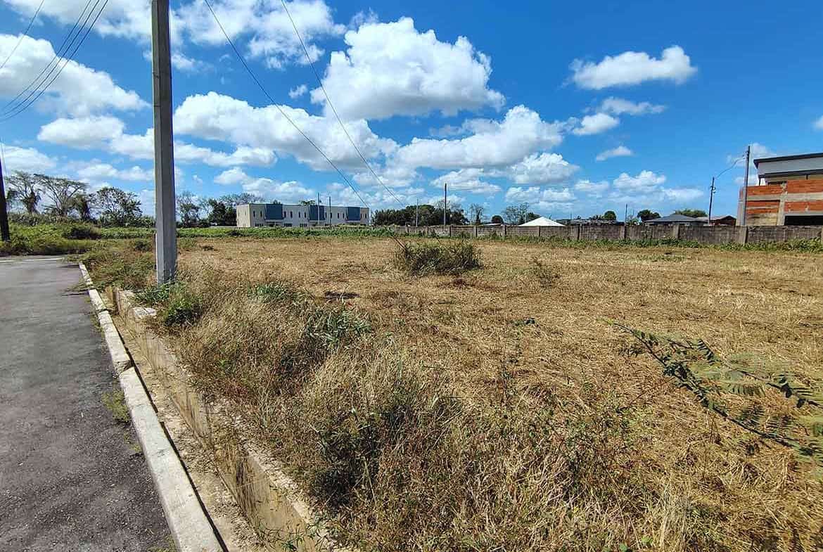 Cornerstone- Vacant land plot in Longdenville with clear sky and nearby buildings.