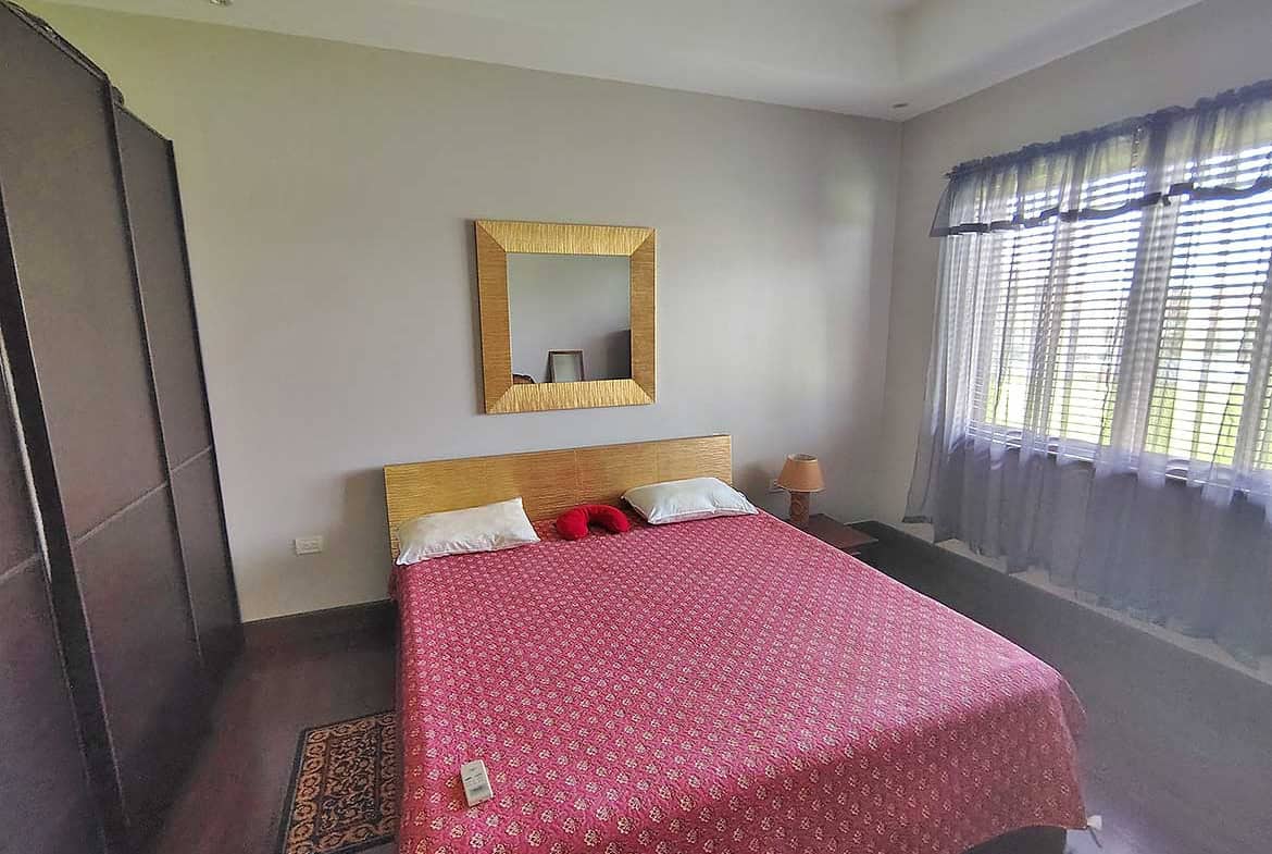 Cornerstone- Cozy bedroom with a large bed, mirror, and window view at Millennium Lakes Home.