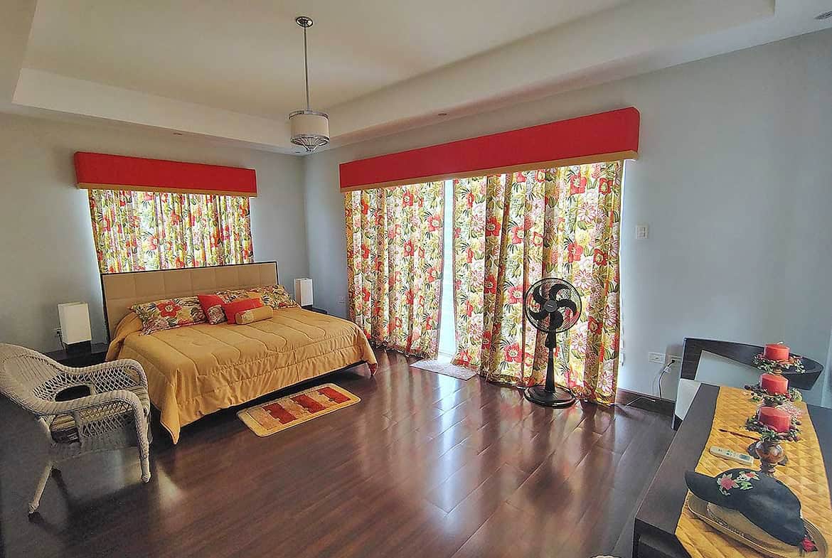 Cornerstone- Spacious bedroom with floral curtains, wooden flooring, and modern decor.