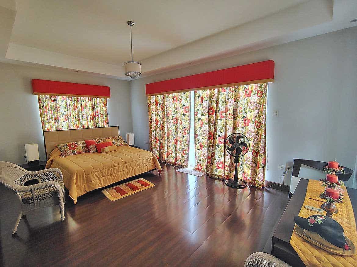 Millennium Lakes Home Bedroom Interior Cornerstone- Spacious bedroom with floral curtains, wooden flooring, and modern decor.