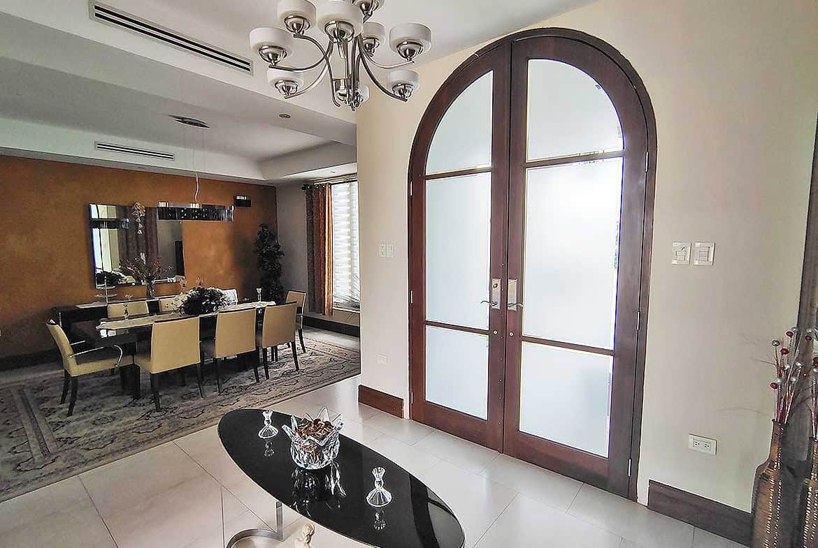 Cornerstone- Stylish arched glass door in modern living space with chandelier and dining area.