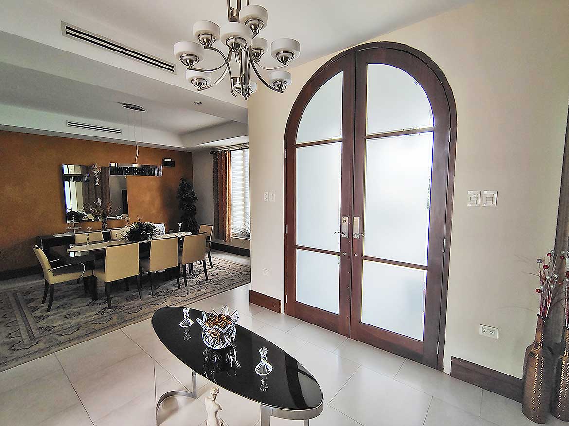 Elegant Home Entrance with Arched Door Cornerstone- Stylish arched glass door in modern living space with chandelier and dining area.