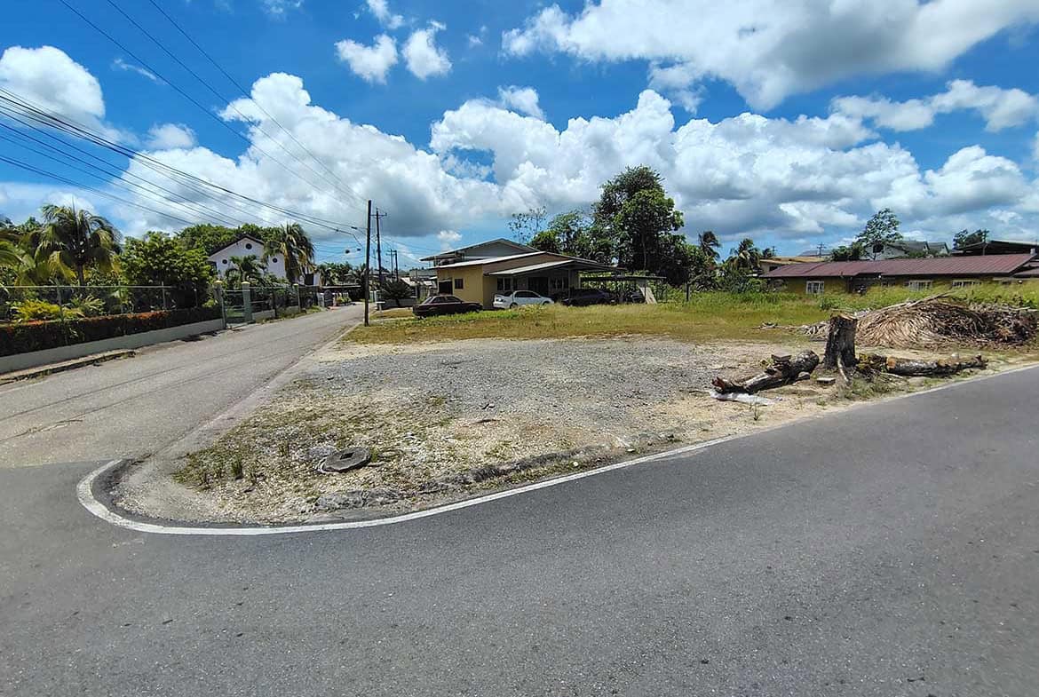 Cornerstone- Empty lot at corner of Ajim Baksh Road with houses and trees nearby.