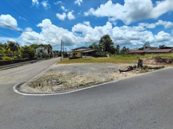 Cornerstone- Empty lot at corner of Ajim Baksh Road with houses and trees nearby.