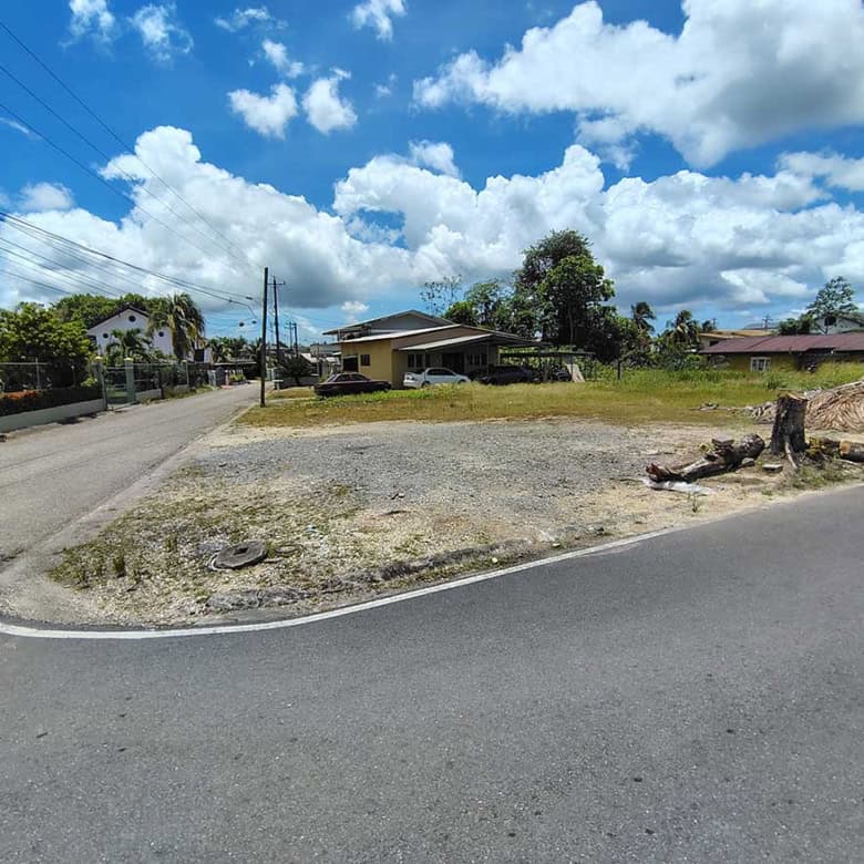 Cornerstone- Empty lot at corner of Ajim Baksh Road with houses and trees nearby.